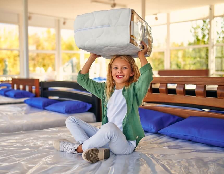 Kind sitzt mit Doppeldecke auf Bett im Duvet-Shop